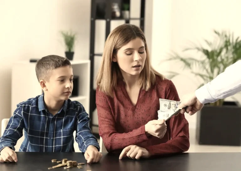 Mother receiving child support payment while sitting at a table with her son, reviewing money during a financial discussion at home.