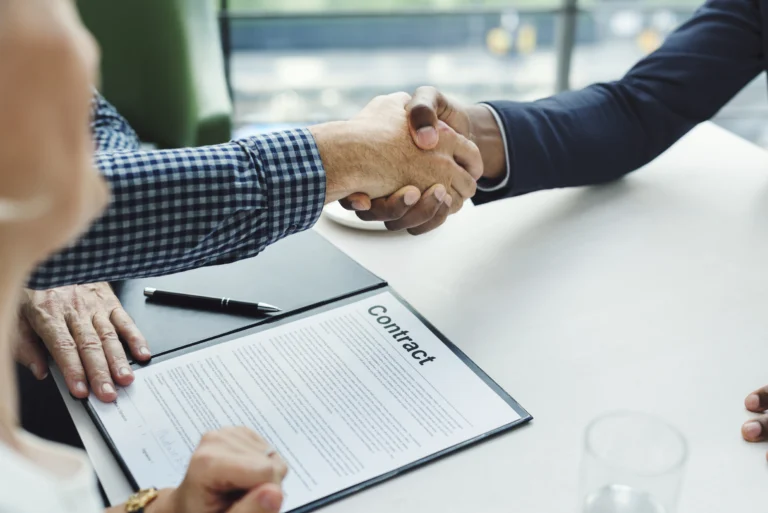 Business handshake over a signed contract on a desk.